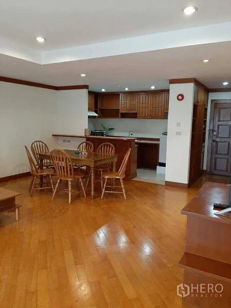 Apartment for rent in Watthana, Bangkok - Open kitchen with wooden cabinetry adjoining the dining area on hardwood flooring.