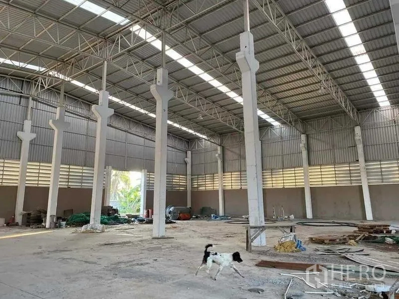 Warehouse for sale in Chon Buri - High-bay warehouse interior featuring steel trusses, skylights, and open concrete floor space.