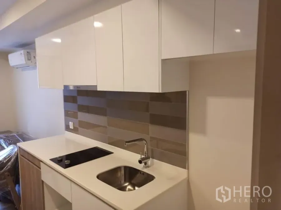 Condominium for sale in Din Daeng, Bangkok - Compact kitchenette with white cabinets, induction hob, sink and striped tile backsplash in Maestro 03 condo.