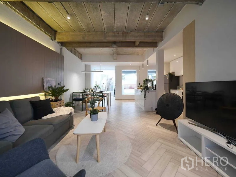 Townhouse for rent in Watthana, Bangkok - Spacious living room with sofa, TV unit, dining area and exposed concrete ceiling.