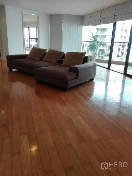 Condominium for rent in Khlong Toei, Bangkok - Second living area with sectional sofa, wraparound windows, and balcony access.