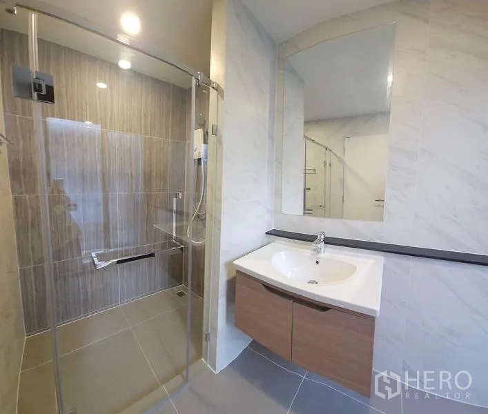 Detached House for rent in Saphan Sung, Bangkok - Modern bathroom featuring a glass-enclosed shower, large mirror and wall-mounted vanity.