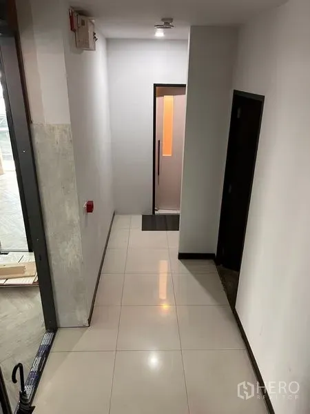 办公空间 出租在Khlong Toei, Bangkok - 整洁走廊，亮面瓷砖地面，左右为房门，尽头为明亮玻璃门。