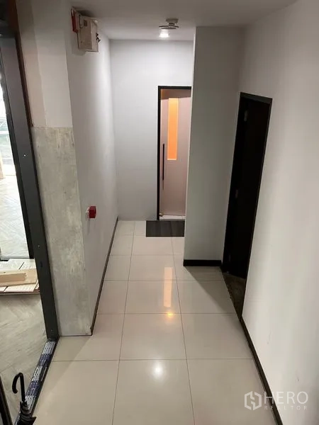 办公空间 出租在Khlong Toei, Bangkok - 整洁走廊，亮面瓷砖地面，左右为房门，尽头为明亮玻璃门。