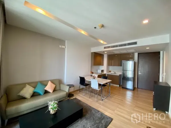 Condominium for rent in Khlong Toei, Bangkok - Open-plan living room connected to a fitted kitchen with stainless refrigerator and dining set.