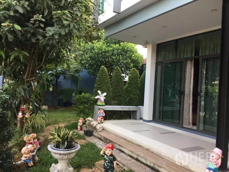 独立式住宅 出售在Pak Kret, Nonthaburi - 前廊与草坪花园，推拉玻璃门、石凳与装饰小雕像。