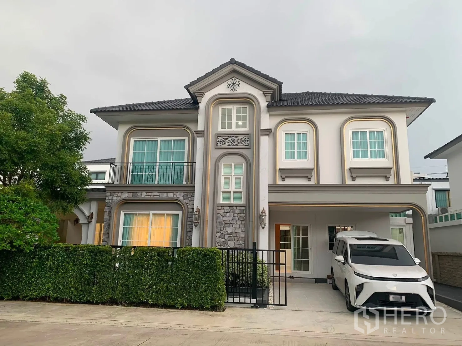 บ้านเดี่ยว for rent in Bang Phli, Samut Prakan - บ้านเดี่ยวสองชั้นด้านหน้า พร้อมรั้วพุ่มไม้และที่จอดรถมีหลังคา.