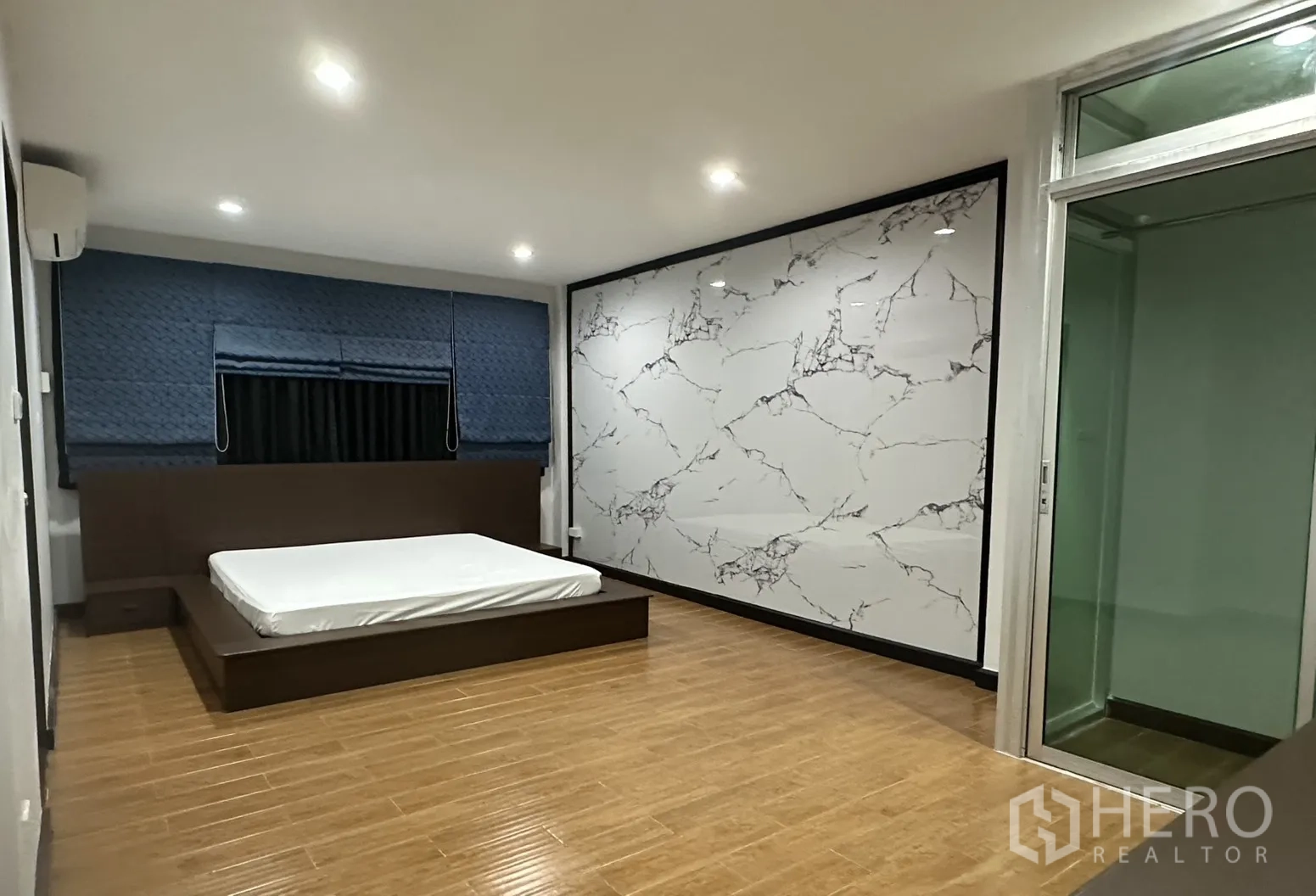 Home Office for rent in Khlong Toei, Bangkok - Large bedroom with platform bed, wood-look flooring, and a sliding glass door.