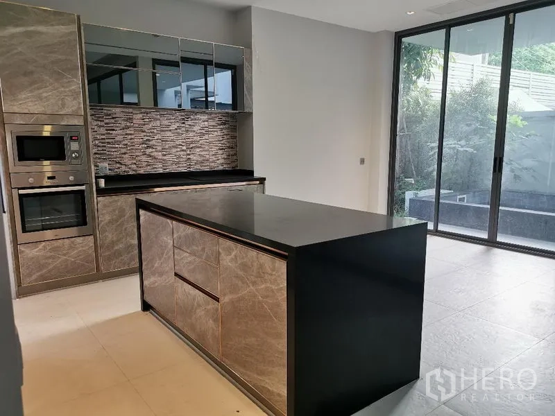 Detached House for sale in Wang Thonglang, Bangkok - Close view of the kitchen island and appliances next to large sliding doors to the patio.