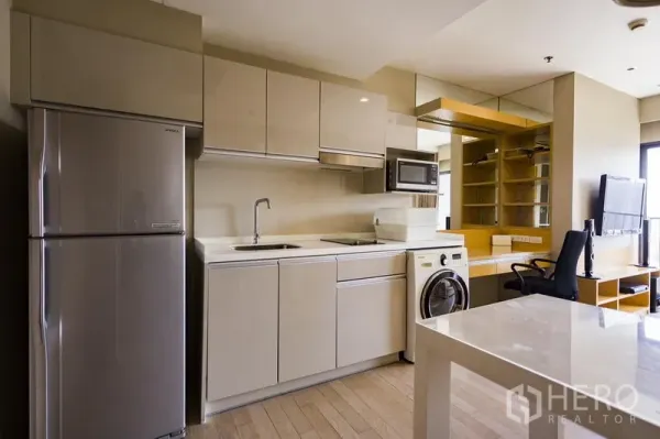 Condominium for rent in Khlong Toei, Bangkok - Modern kitchenette with glossy cabinets, fridge, microwave and front-load washer next to work desk and shelving.
