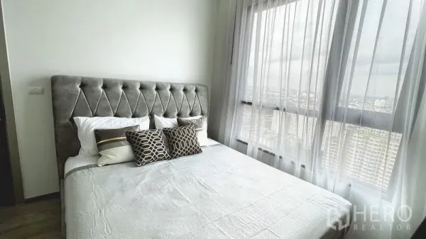 公寓 出租在Watthana, Bangkok - 主卧配软包靠背、高挑窗与纱帘，可远眺城市景观。