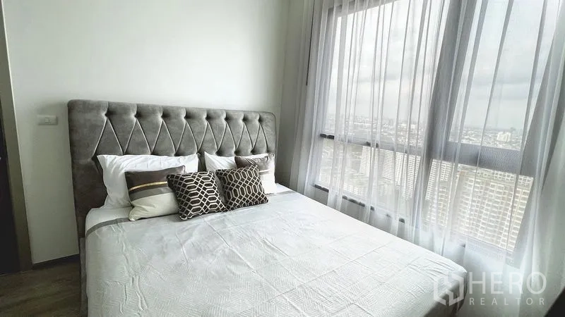 公寓 出租在Watthana, Bangkok - 主卧配软包靠背、高挑窗与纱帘，可远眺城市景观。