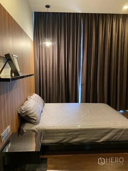Condominium for rent in Watthana, Bangkok - Cozy bedroom with wood accent wall, bedside shelf, soft lighting and blackout floor-to-ceiling curtains.