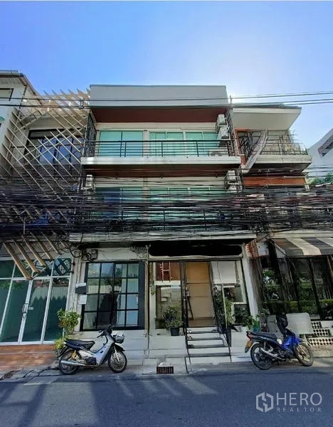 Shophouse for sale in Bang Rak, Bangkok - Four-storey shophouse facade with glass balconies and streetfront entrance, scooters parked outside.