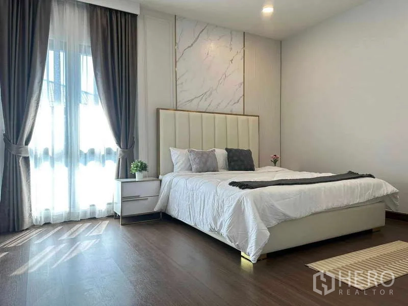 Detached House for rent or sale in Bang Phli, Samut Prakan - Bright master bedroom with marble accent wall, padded headboard, floor-to-ceiling curtains and wood flooring.