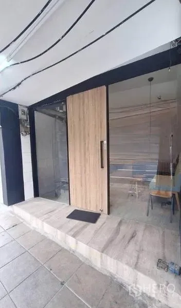 零售空间 出租在Watthana, Bangkok - 玻璃门店入口，木门与前方瓷砖外廊，适合设置招牌。