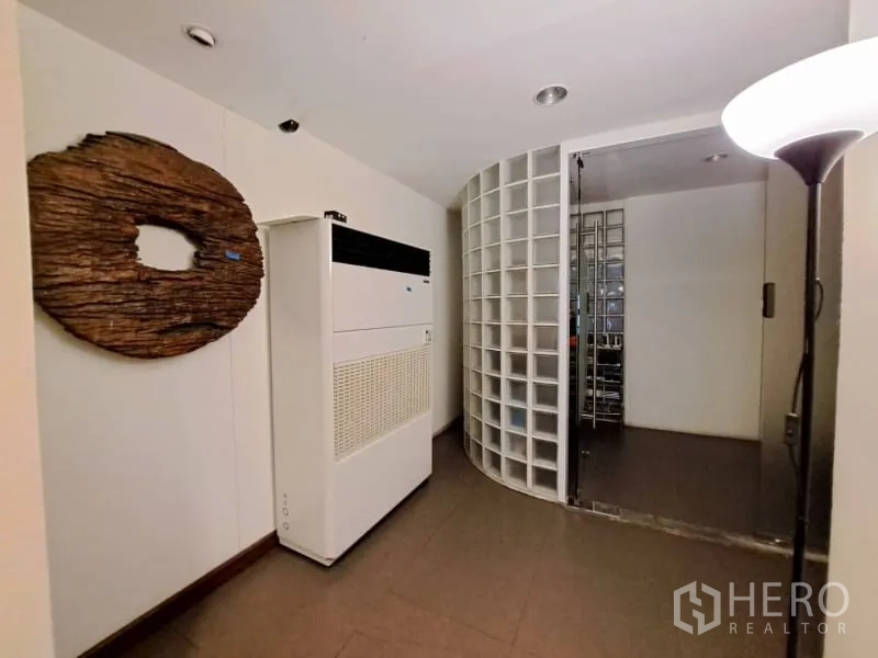 Shophouse for rent in Watthana, Bangkok - Hall with AC unit and curved glass-block wall leading to storage room.