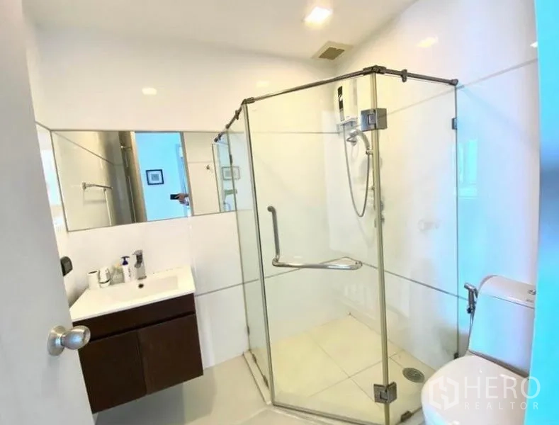 Condominium for rent in Huai Khwang, Bangkok - Guest bathroom with corner glass shower enclosure and white tiles.