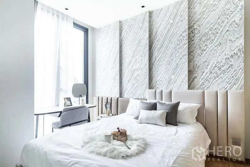 Condominium for rent in Khlong Toei, Bangkok - Bright second bedroom with textured wall panels, soft headboard, and study desk by a large window.