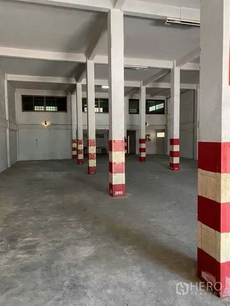 Warehouse for rent in Phasi Charoen, Bangkok - Interior aisle with safety-marked pillars and wall-mounted lighting in a warehouse.