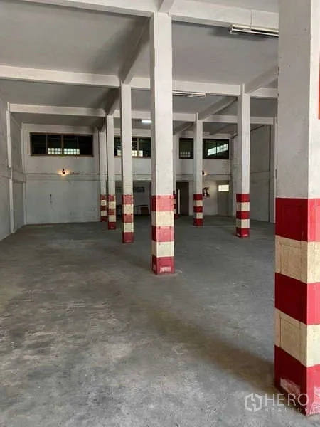 Warehouse for rent in Phasi Charoen, Bangkok - Interior aisle with safety-marked pillars and wall-mounted lighting in a warehouse.