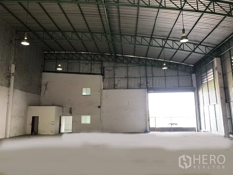 工厂 出租在Pathum Thani - 仓库内部朝向大型卷门，可见附建办公区与高挑屋顶。