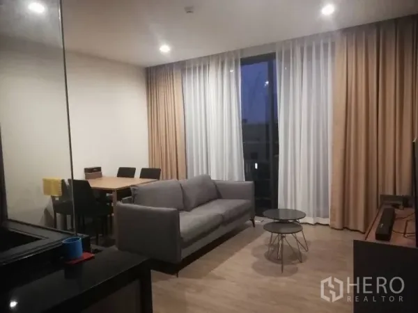 คอนโด ให้เช่าในWatthana, Bangkok - ห้องนั่งเล่นหันไปทางชั้นวางทีวี พร้อมโซฟาสีเทา ชุดโต๊ะทานอาหาร และผ้าม่านโปร่งสูง