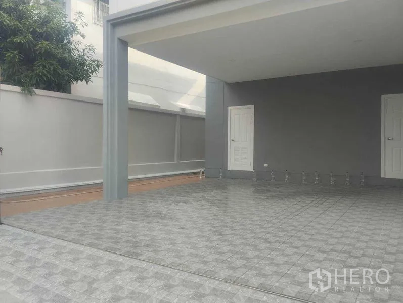 Detached House for sale in Phra Khanong, Bangkok - Spacious covered carport with patterned tiles and storage doors at the back.