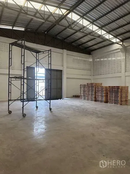 Warehouse for rent in Suan Luang, Bangkok - Spacious warehouse interior with high steel truss roof, concrete floor, and a large sliding loading door.