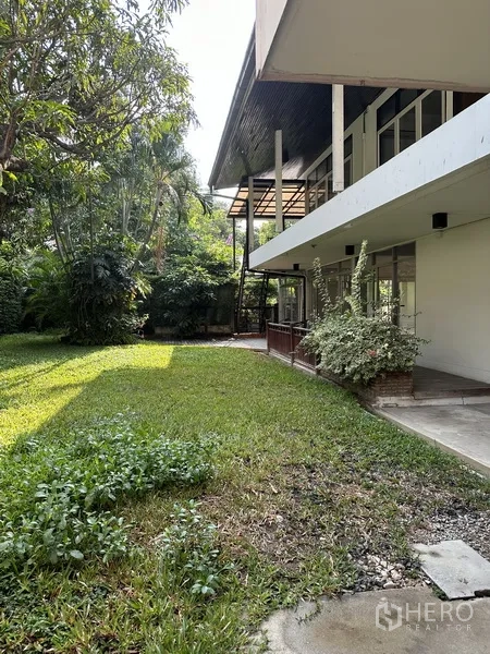 独立式住宅 出租在Khlong Toei, Bangkok - 房屋侧院，浓密树木与草坪沿白色两层楼