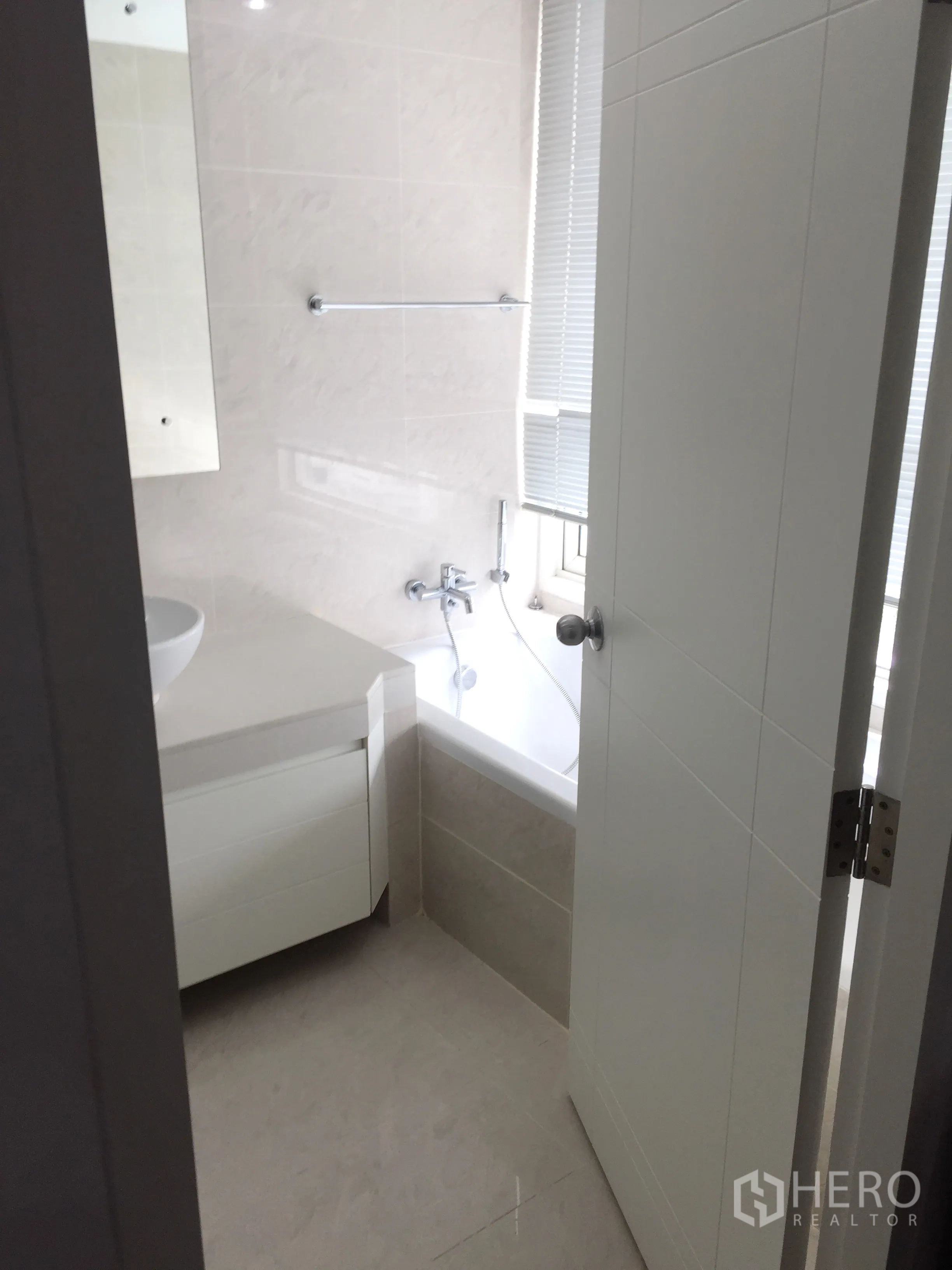 Condominium for rent in Khlong Toei, Bangkok - Light-tiled bathroom with a bathtub by the window and a white vanity unit.