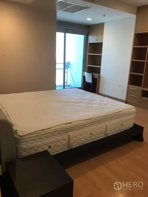 Condominium for rent in Khlong Toei, Bangkok - Spacious second bedroom with large bed, built-in shelving, desk and balcony access.