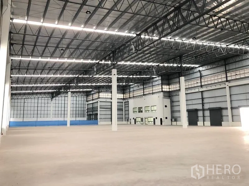 Factory for rent in Samut Prakan - Expansive high‑clearance warehouse hall with steel truss roof, polished concrete floor and internal office block.
