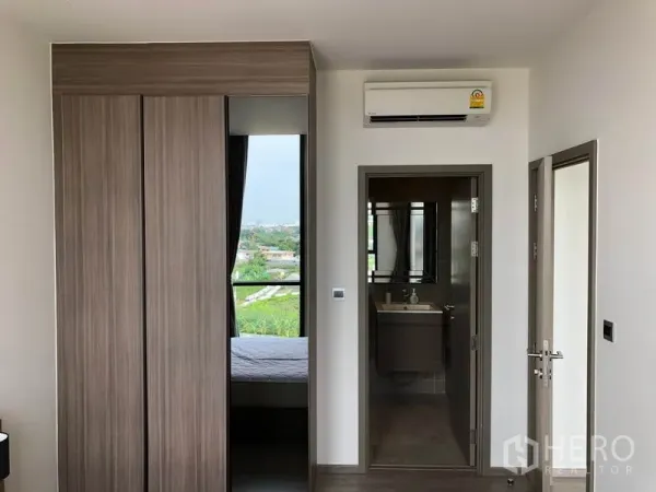 Condominium for rent in Watthana, Bangkok - Bedroom entry with built‑in sliding wardrobe, air conditioner, and door to the bathroom.