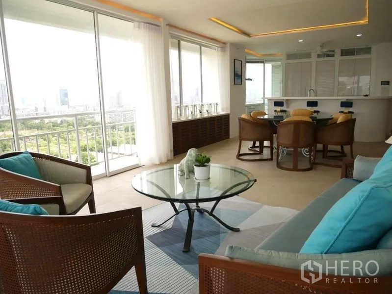 Condominium for rent in Khlong Toei, Bangkok - Living area with glass coffee table and balcony facing a park and city skyline.