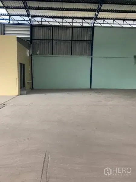 Factory for rent in Khlong Luang, Pathum Thani - Warehouse interior with smooth concrete floor, metal walls, high roof truss, and an attached utility/bathroom block.