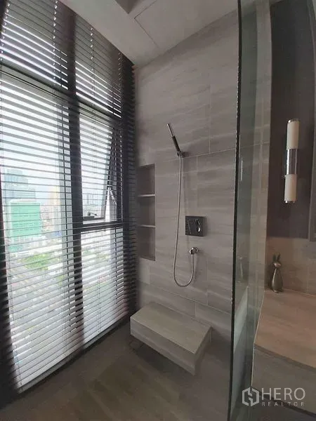 公寓 出售在Bang Rak, Bangkok - 步入式淋浴间，灰色瓷砖与内置座椅，落地窗配百叶可观城市景观。