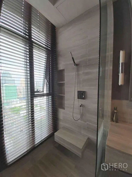 公寓 出售在Bang Rak, Bangkok - 步入式淋浴间，灰色瓷砖与内置座椅，落地窗配百叶可观城市景观。