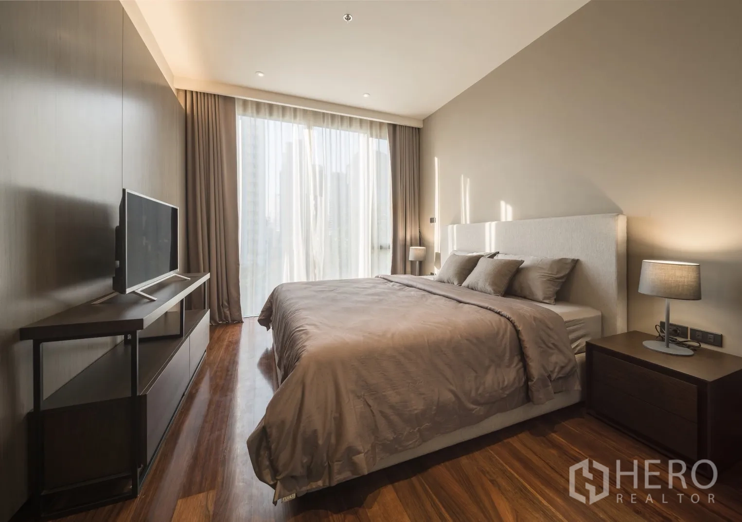 Condominium for rent in Khlong Toei, Bangkok - Sunlit bedroom with large bed, desk and full-height windows with blackout drapes.