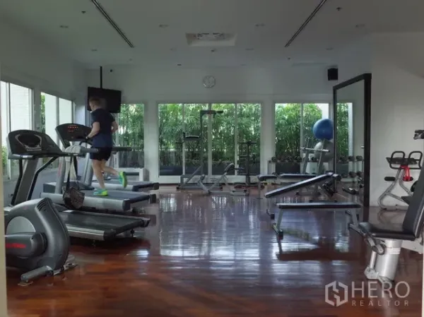 Condominium for rent in Watthana, Bangkok - Bright condo fitness room with treadmills, weight machines and wood flooring facing greenery.