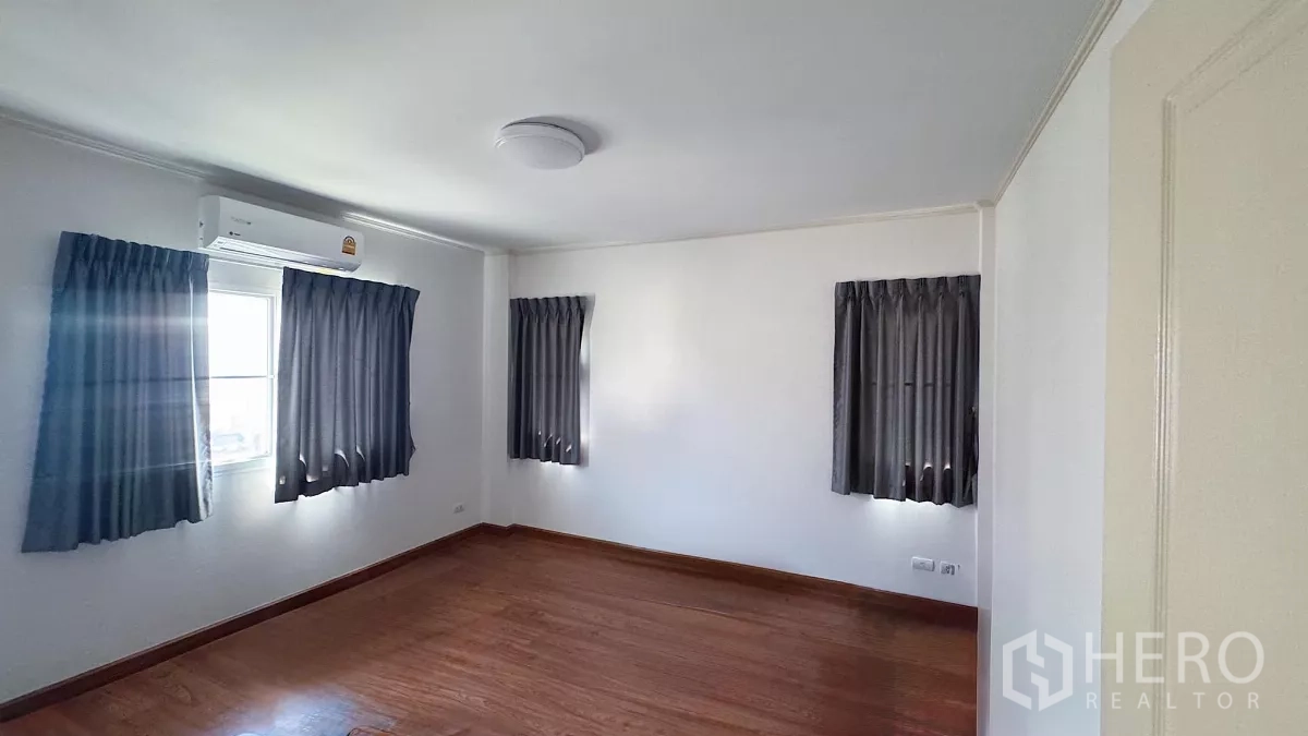 Detached House for sale in Lat Krabang, Bangkok - Corner bedroom with multiple windows, wood floors, air conditioning and grey curtains.