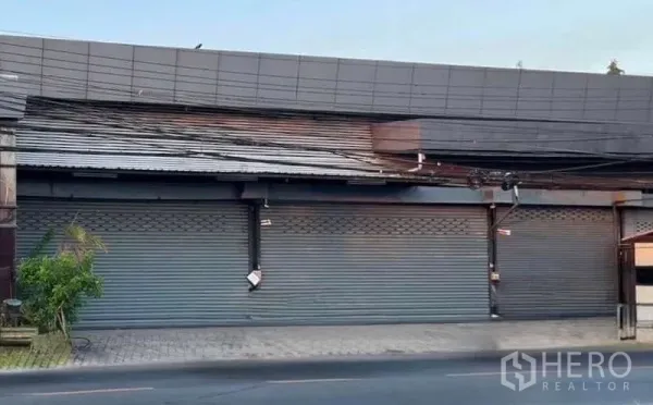 Warehouse for rent in Lat Phrao, Bangkok - Street‑facing warehouse frontage with multiple metal roller shutters and a wide pavement.