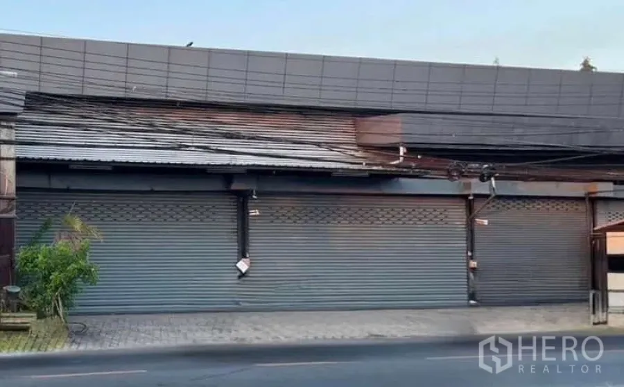 Warehouse for rent in Lat Phrao, Bangkok - Street‑facing warehouse frontage with multiple metal roller shutters and a wide pavement.