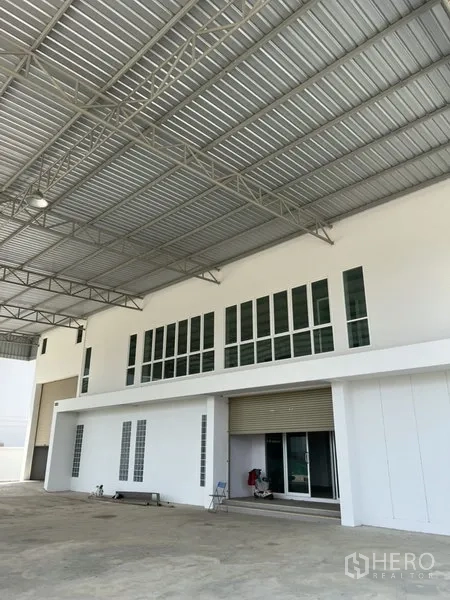 工厂 出租或出售在Bang Bo, Samut Prakan - 底层装卸区，配电动卷帘门与二层办公室窗户，位于钢结构雨棚下。