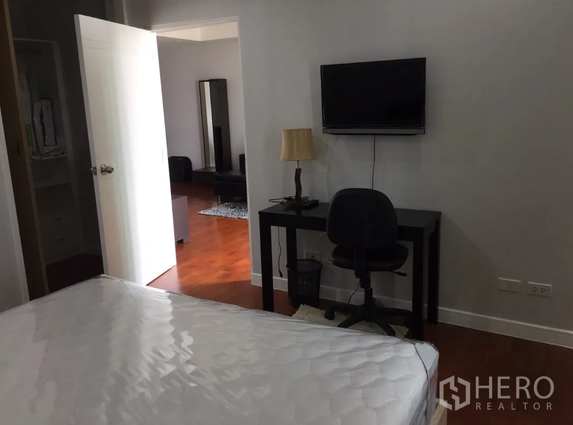 Condominium for rent in Khlong Toei, Bangkok - Bedroom with wood flooring, a work desk and wall-mounted TV, looking toward the living area.
