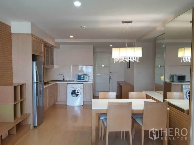 公寓 出租在Watthana, Bangkok - 曼谷公寓的开放式客餐厅，水晶吊灯、镜面墙，配备带洗衣机和不锈钢冰箱的内置厨房。