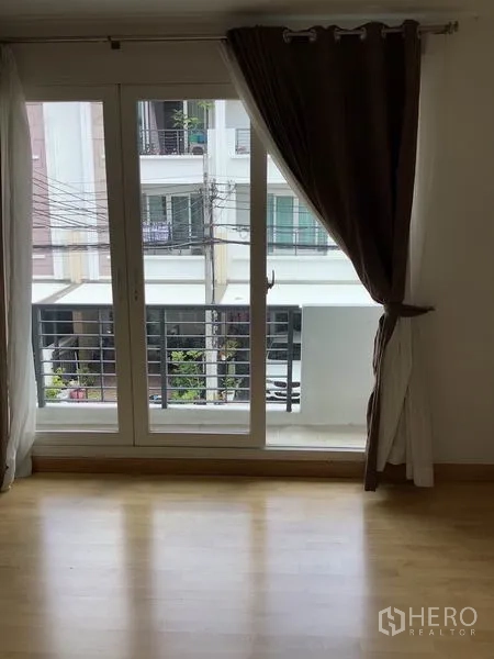 联排别墅 出租或出售在Wang Thonglang, Bangkok - 卧室设推拉玻璃门通阳台，木地板与深色窗帘。