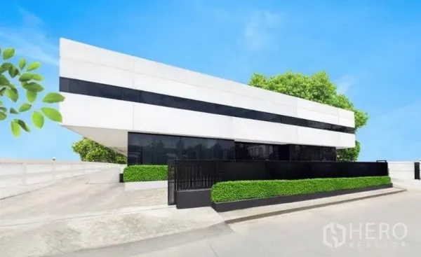货栈 出租在Bang Phli, Samut Prakan - 现代白色工业建筑外观，黑色带状窗、安保大门与修剪绿篱。
