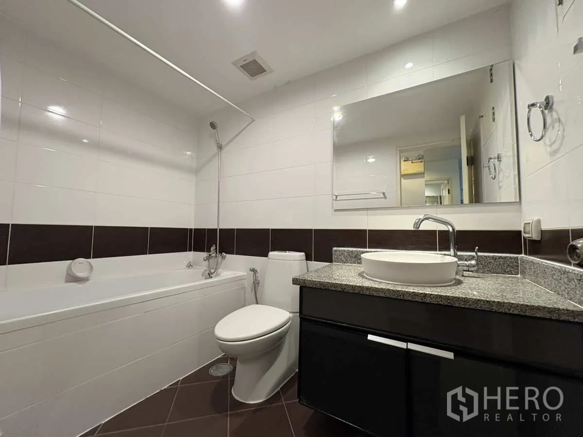 Condominium for rent in Khlong Toei, Bangkok - Clean bathroom with bathtub and shower, countertop basin and large mirror.
