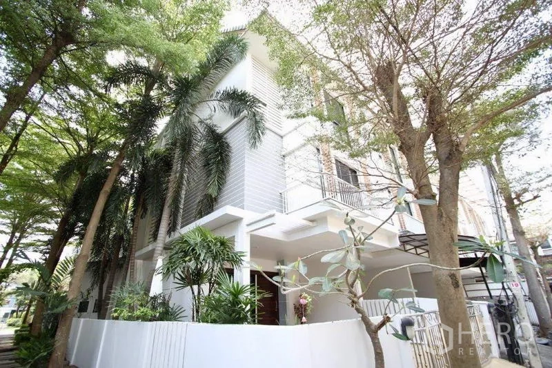 Townhouse for sale in Suan Luang, Bangkok - Corner townhouse exterior with white fence and lush palms along a tree-lined street.